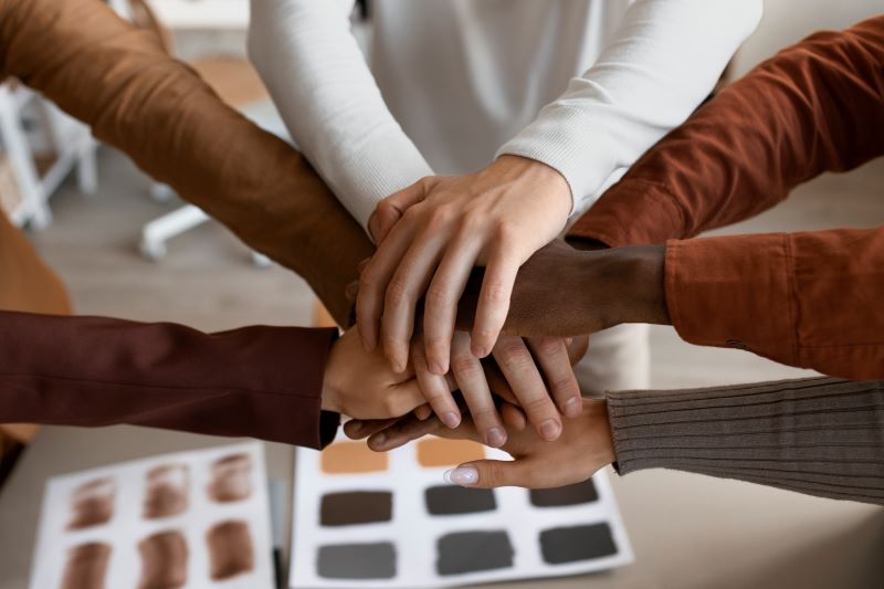 Image depicting a diverse group of people of different races, ages, and backgrounds joining hands in unity, symbolizing the importance of understanding implicit bias and working together to mitigate its impact in a harmonious workplace.